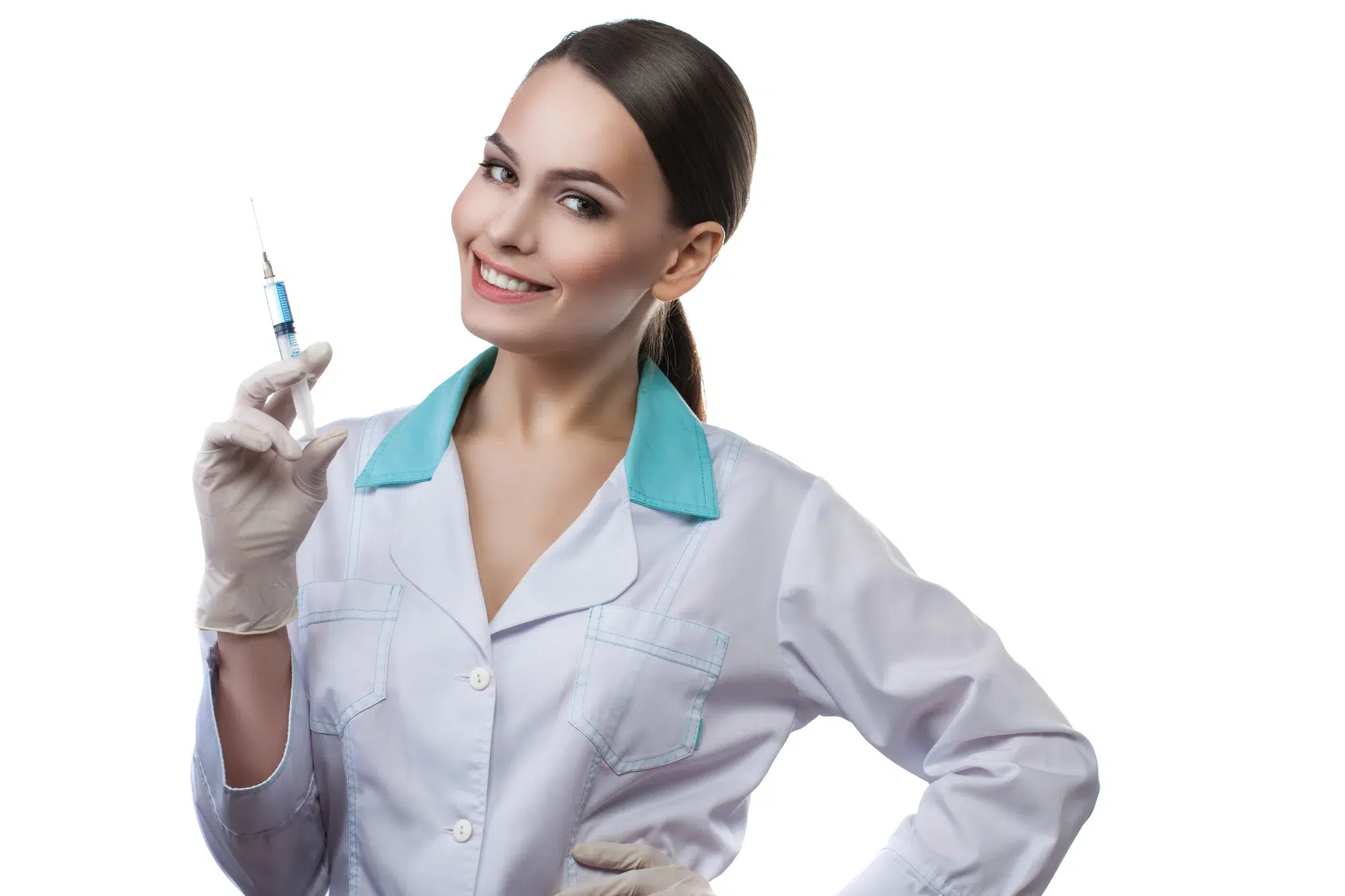 A smiling woman in a white medical coat and gloves holds up a syringe filled with blue liquid. She has dark hair pulled back in a ponytail and stands against a plain white background, ready to administer Botox for Anal Fissure treatment.