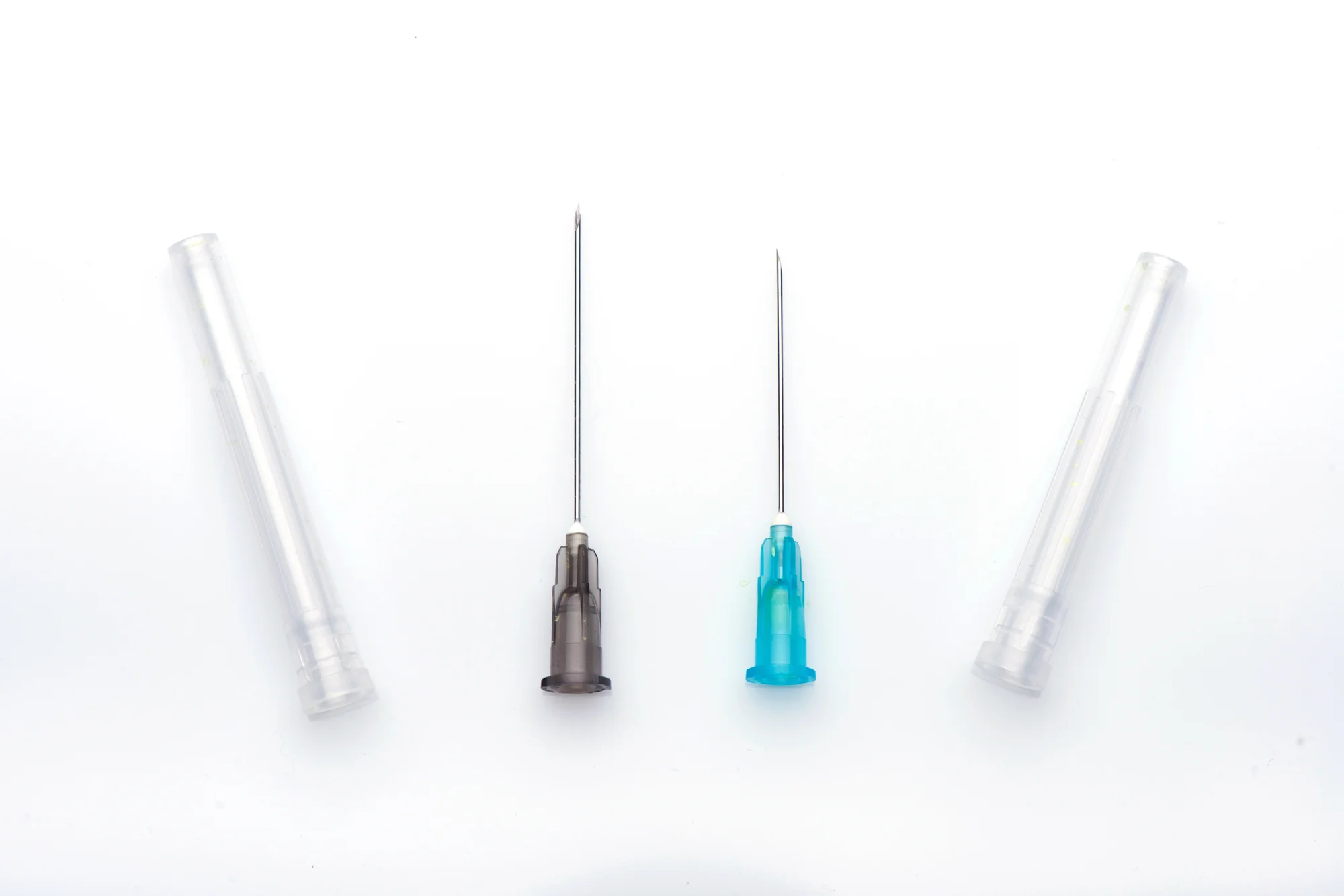 Two hypodermic needles with protective caps placed beside them on a white background showcase the distinct differences in cannula vs. needles for dermal filler injections. The needle on the left has a brown base, while the one on the right features a blue base.