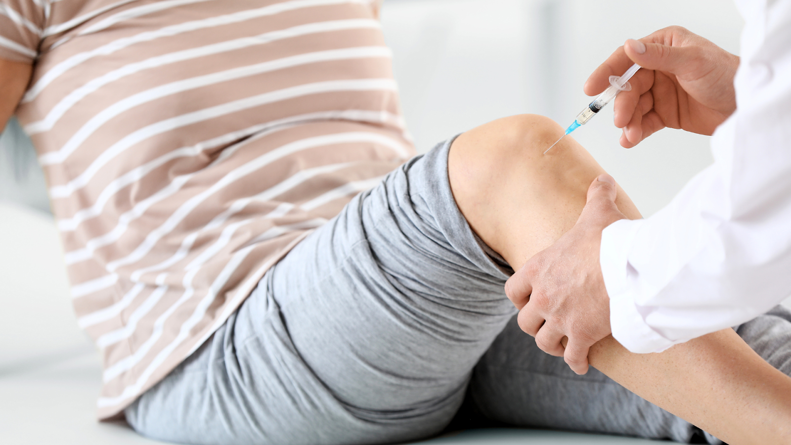 A medical professional injecting a treatment into a patient's knee.