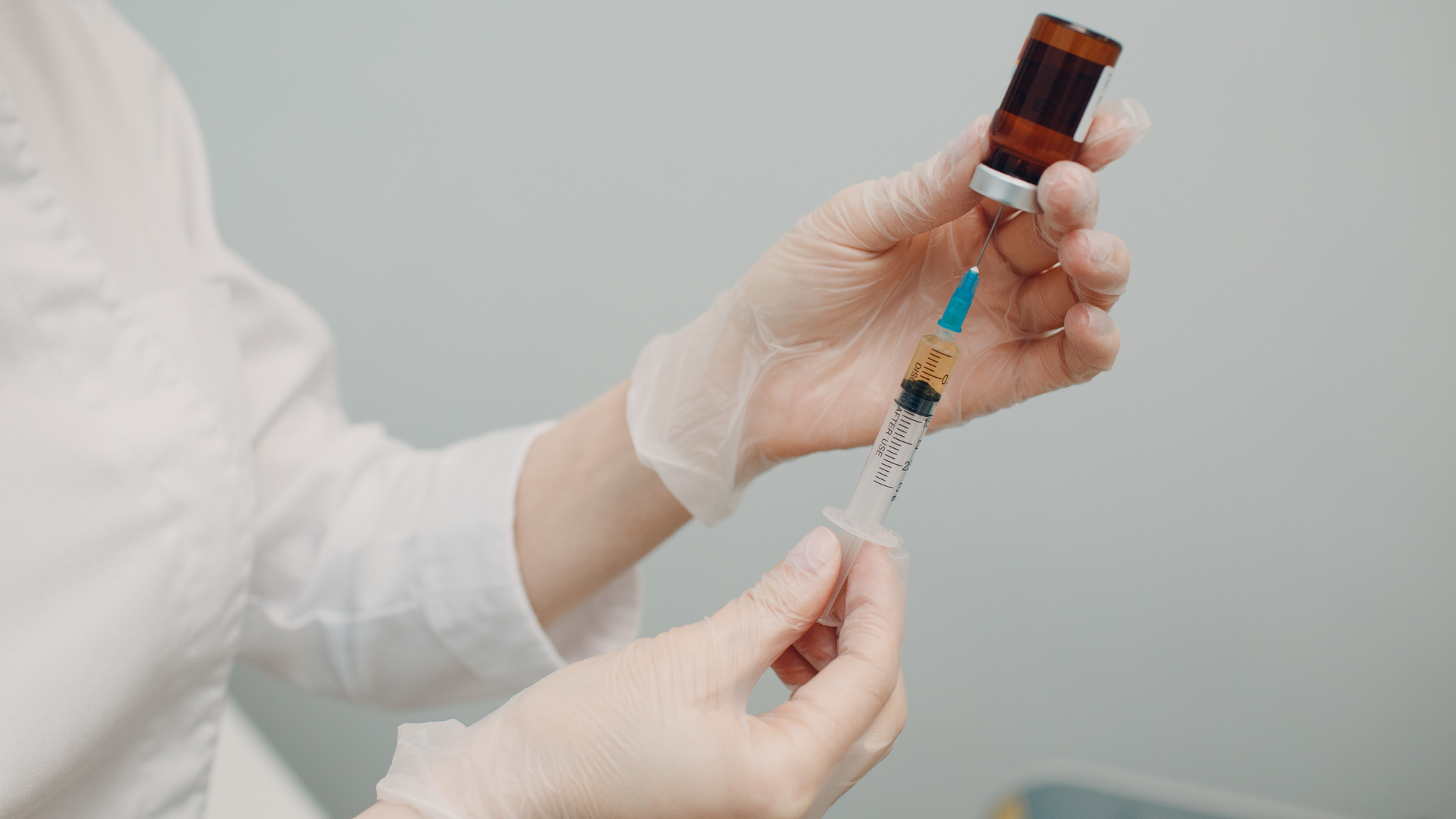 A medical professional transferring the vial contents to the syringe.