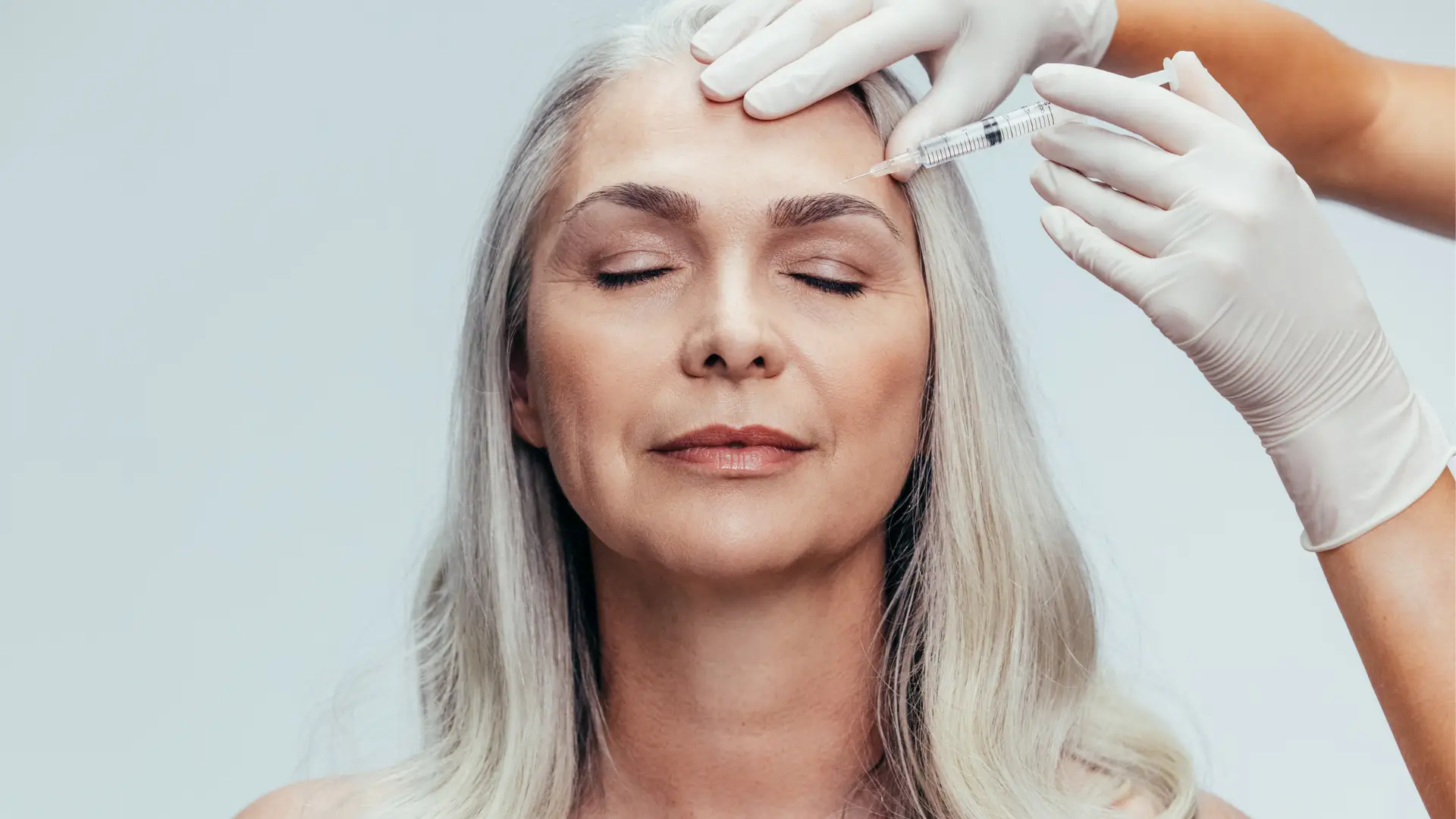 A healthcare professional administering an injection above the eyebrows.