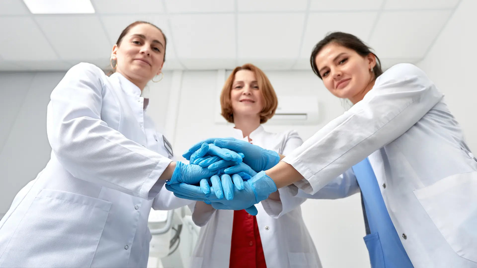 Three medical professionals joining hands while being optimistic.