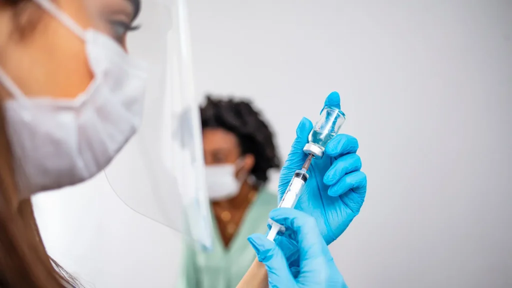 A healthcare provider preparing the medical syringe before injection.