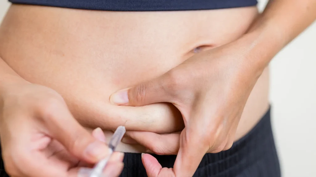 An individual administering an injection into their abdomen.