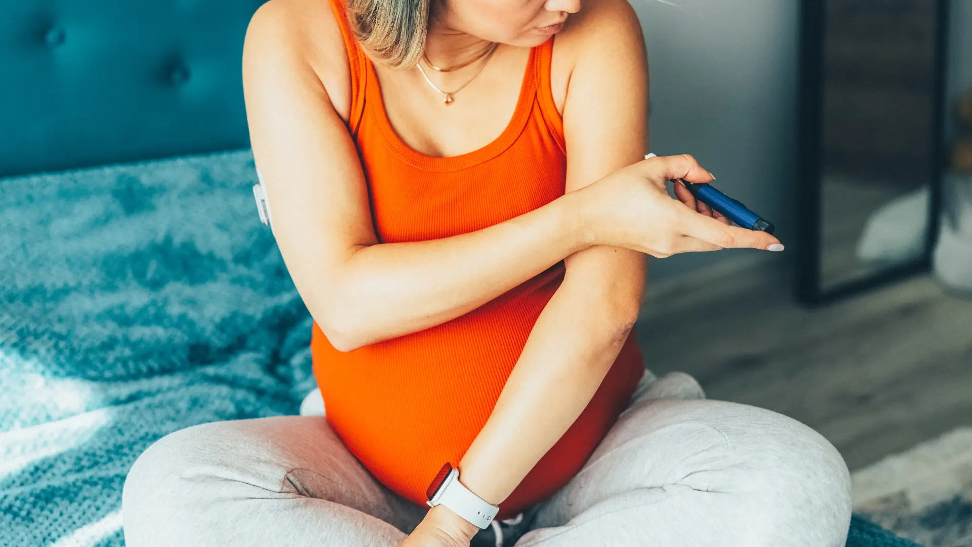 A pregnant individual administering a shot on their upper arm.