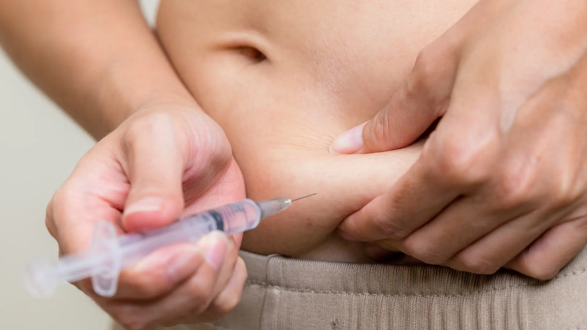 An individual administering a shot into their abdomen.