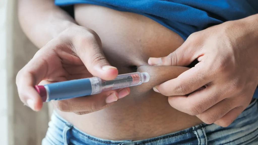 An individual administering a shot on their abdomen.