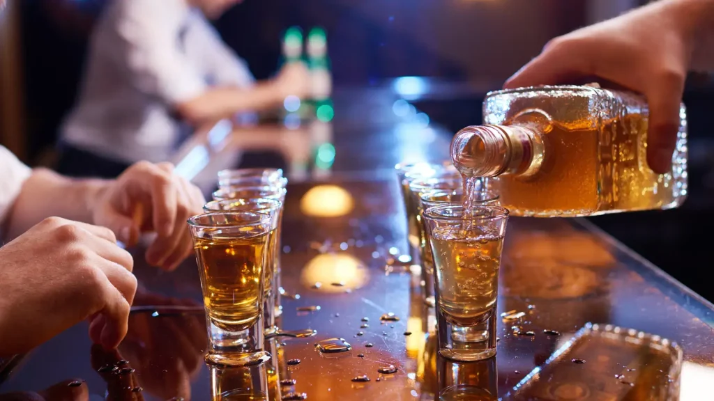A bartender refilling the shot glasses with more liquor.