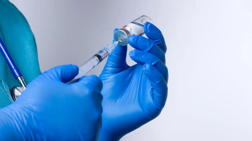 A medical professional transferring the vial's solution to the syringe.