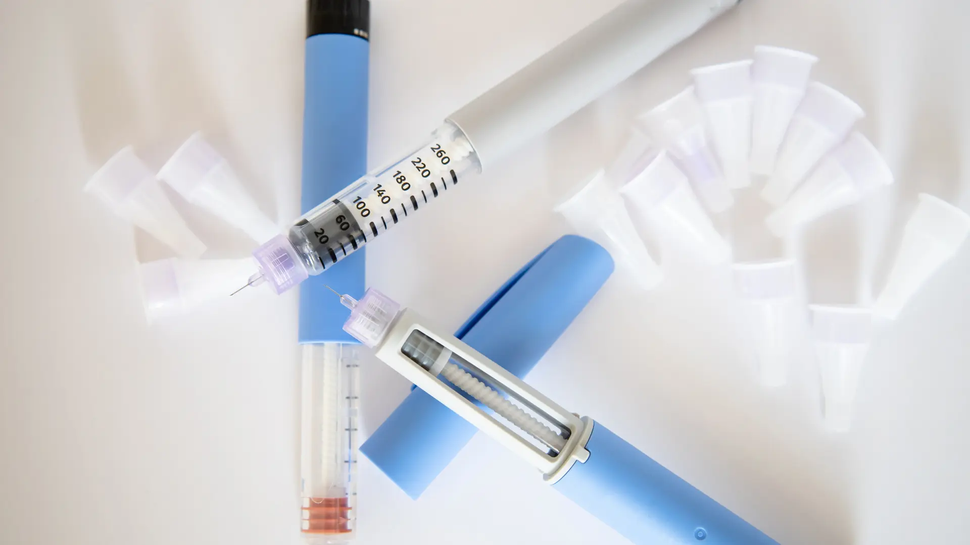 Two injectable pens and caps on a surface.