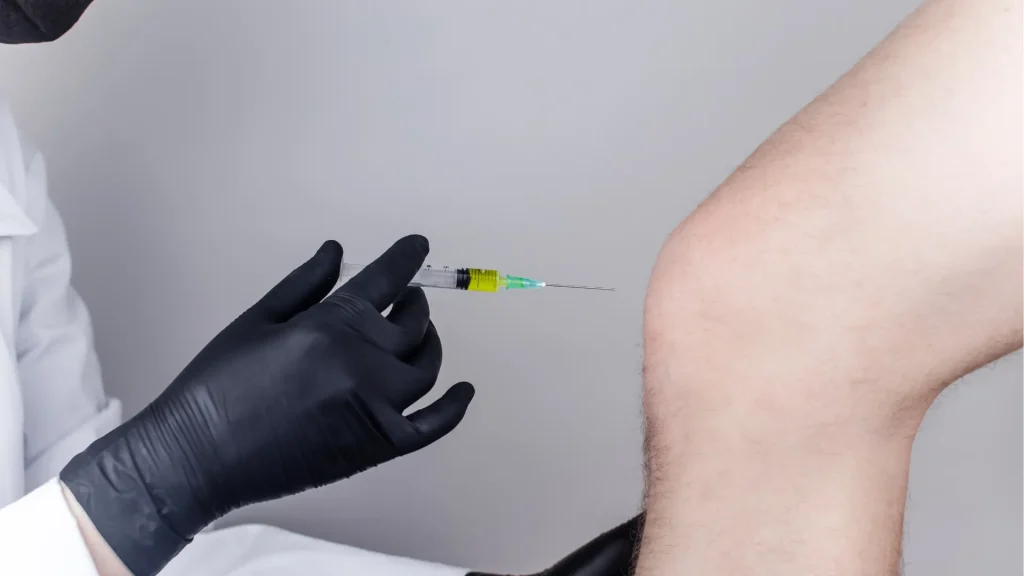 A medical practitioner administering a knee injection.