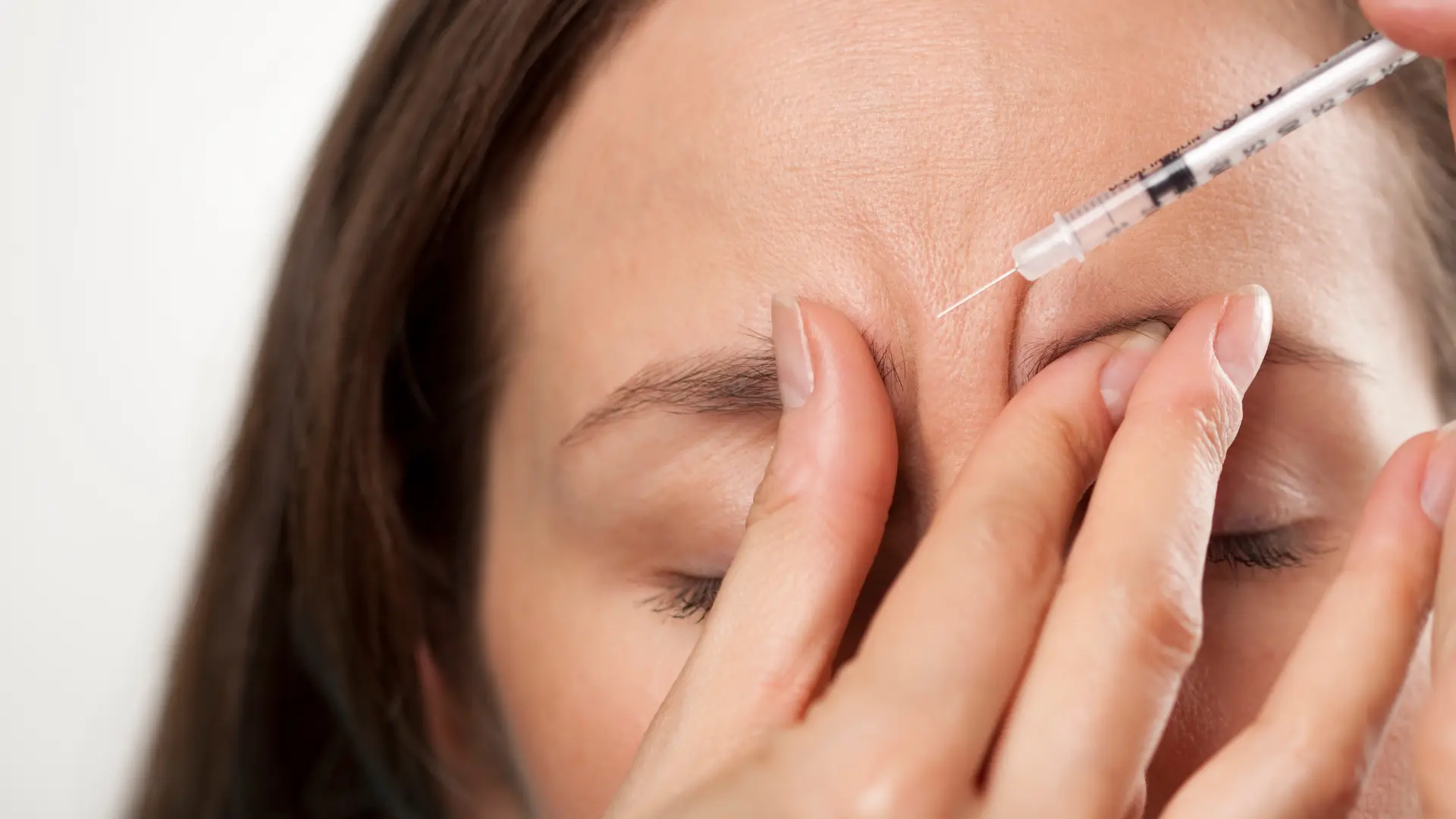 An individual receiving an injection into their frown lines.