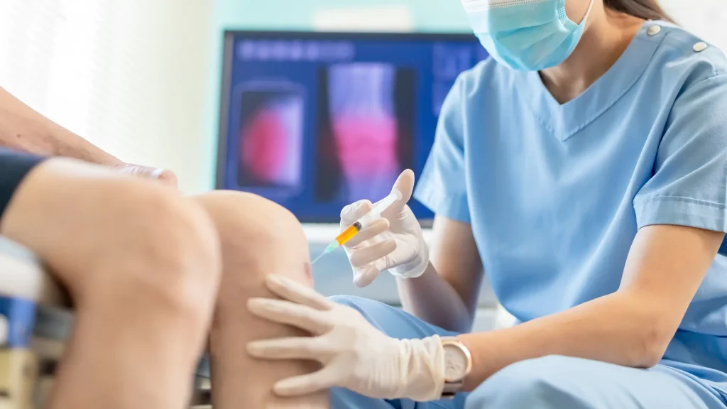 A medical practitioner administering a knee injection.