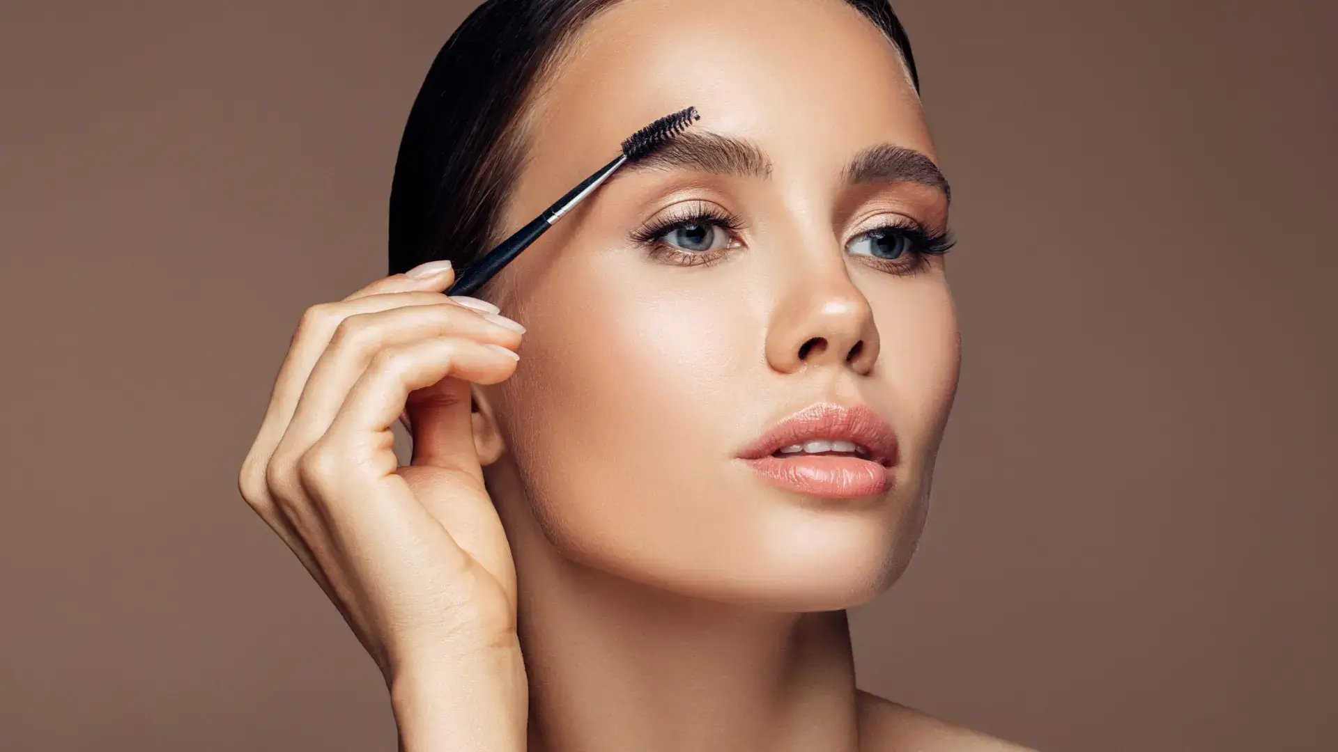 An individual brushing their eyebrows for a thicker, darker look.