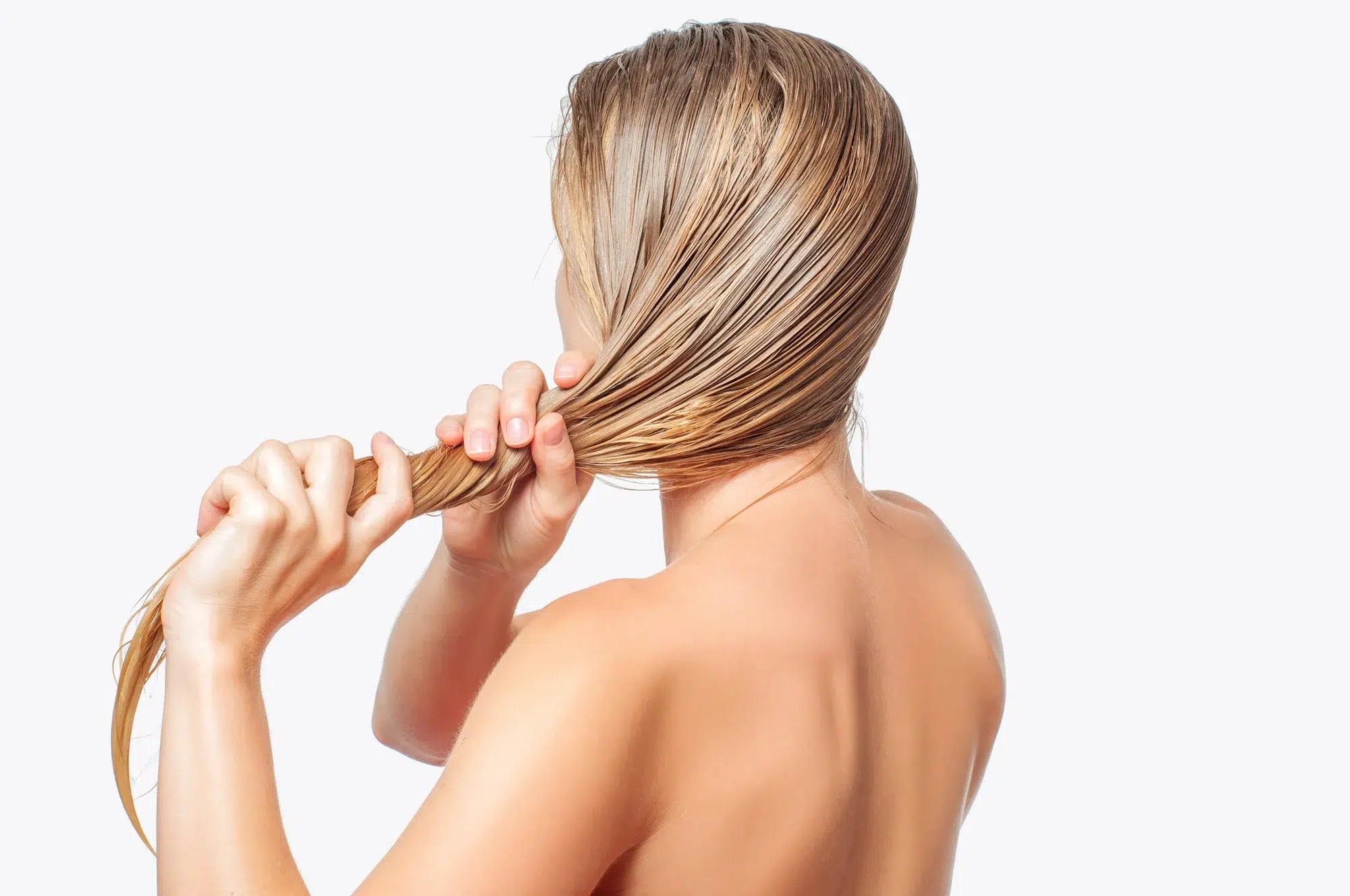 A person with long, wet blonde hair is facing away from the camera and braiding their hair. They are holding their hair in both hands, and only their back and arms are visible against a white background.
