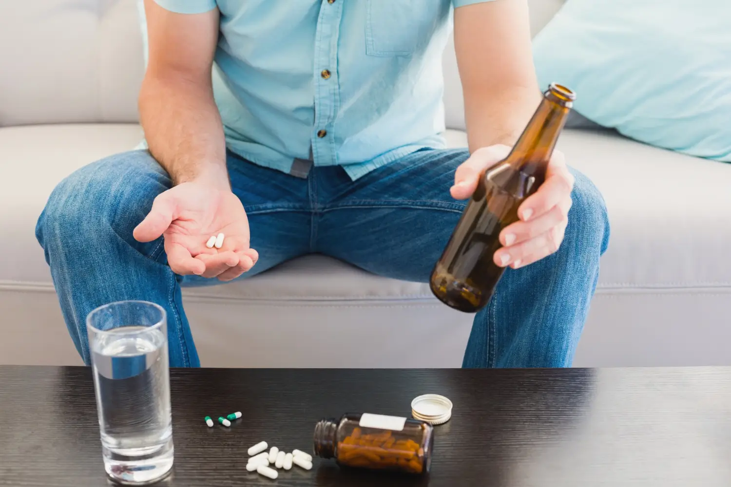An individual holding a bottle of alcohol and their medication tablets.