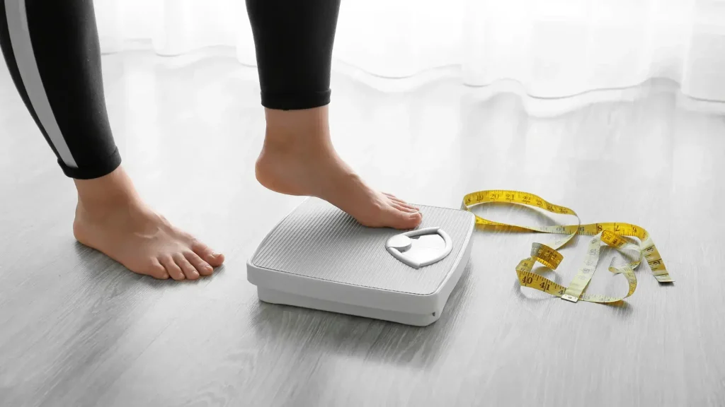 An individual stepping onto a weighing scale.