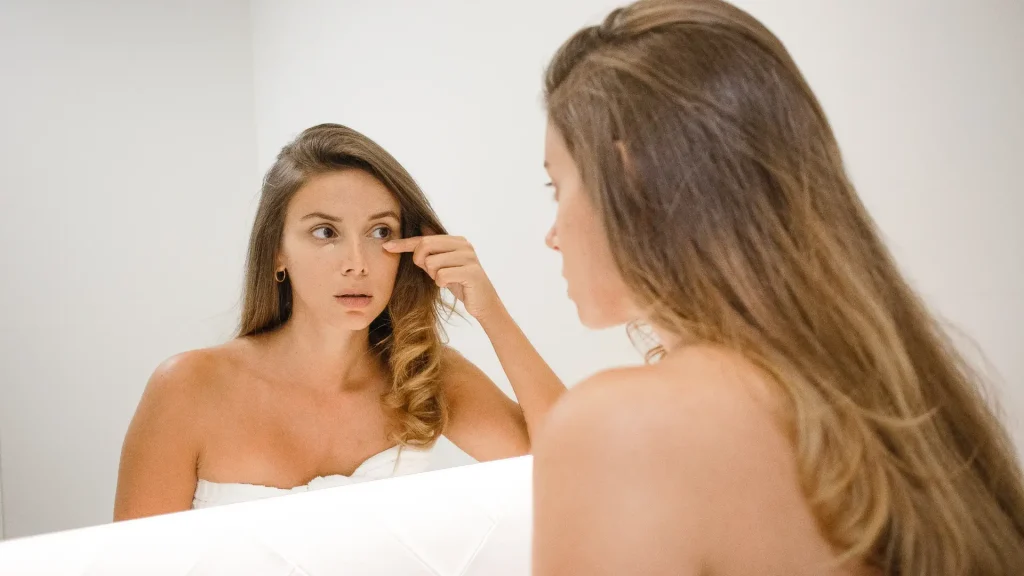 An individual examining their under eye area on the mirror.