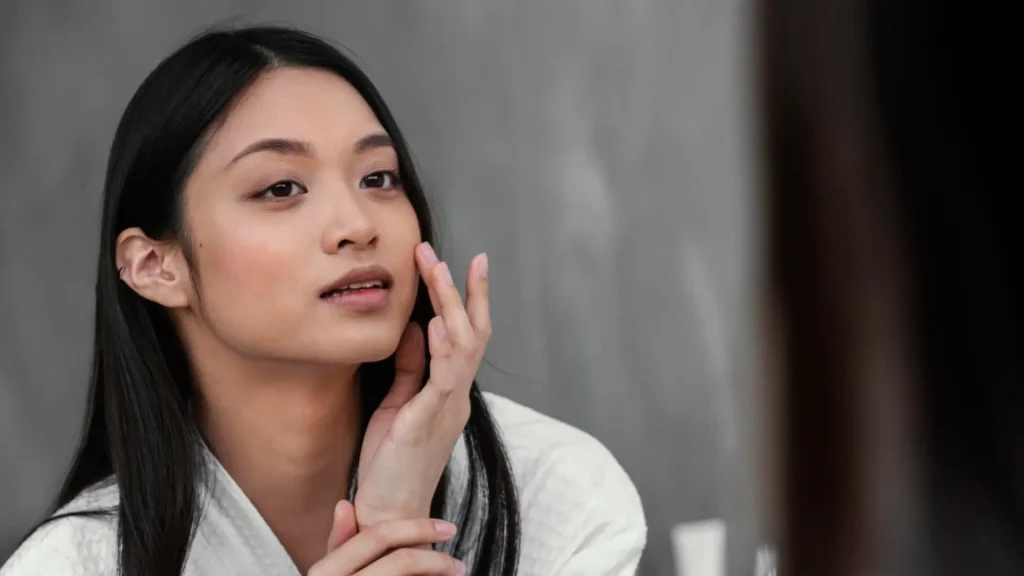 An individual looking at their smooth, clear skin in the mirror.