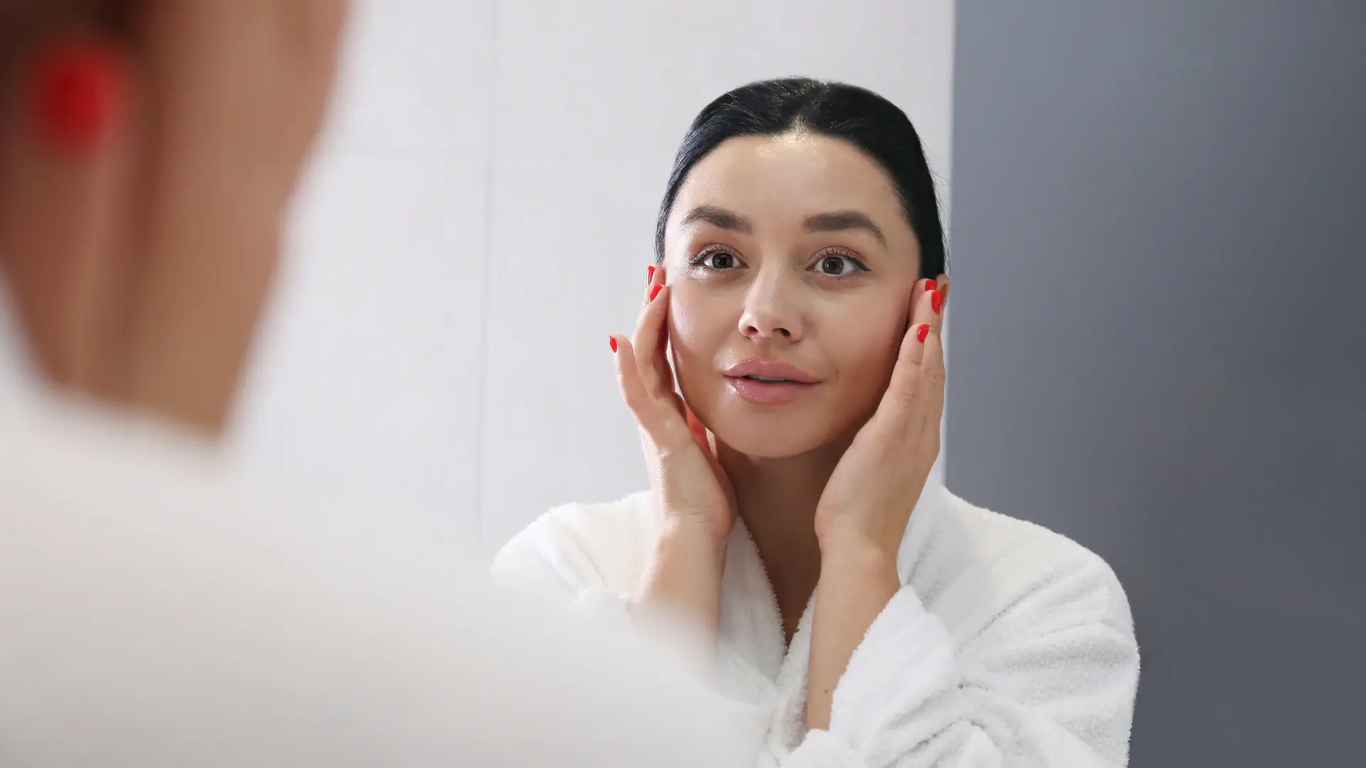 An individual looking at herself in the mirror after their skincare routine.