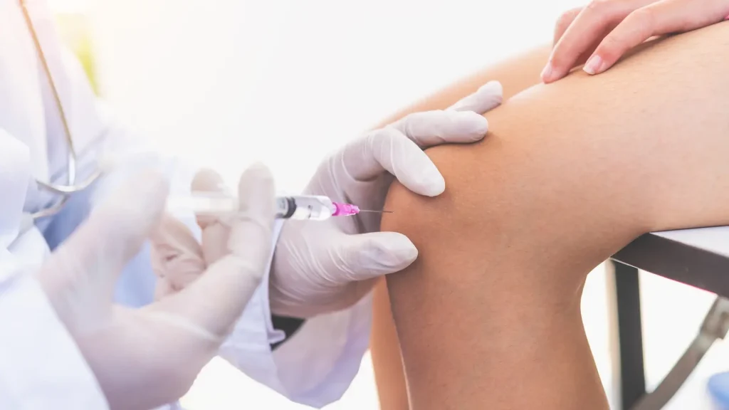 A medical professional administering a knee injection into a patient.