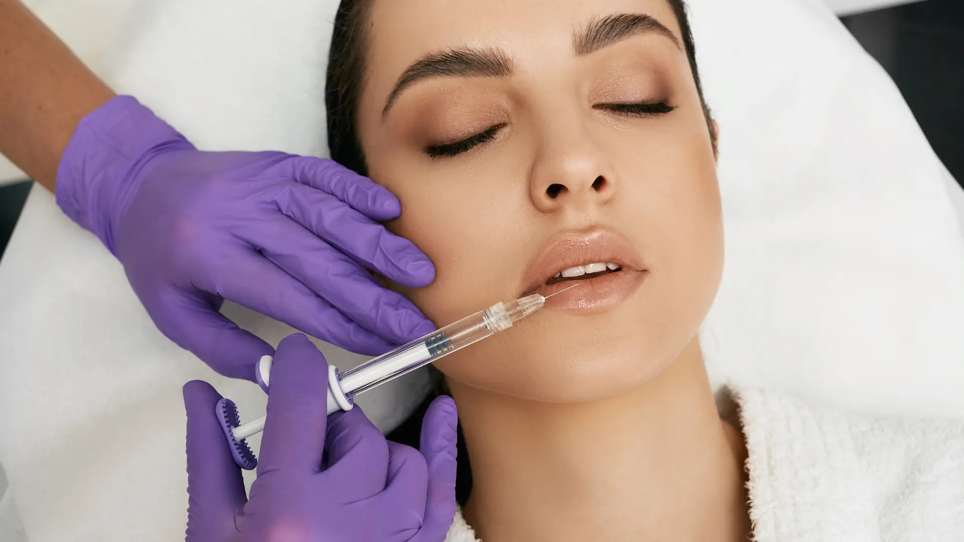 An aesthetic provider administering a dermal filler injection a patient's lips.