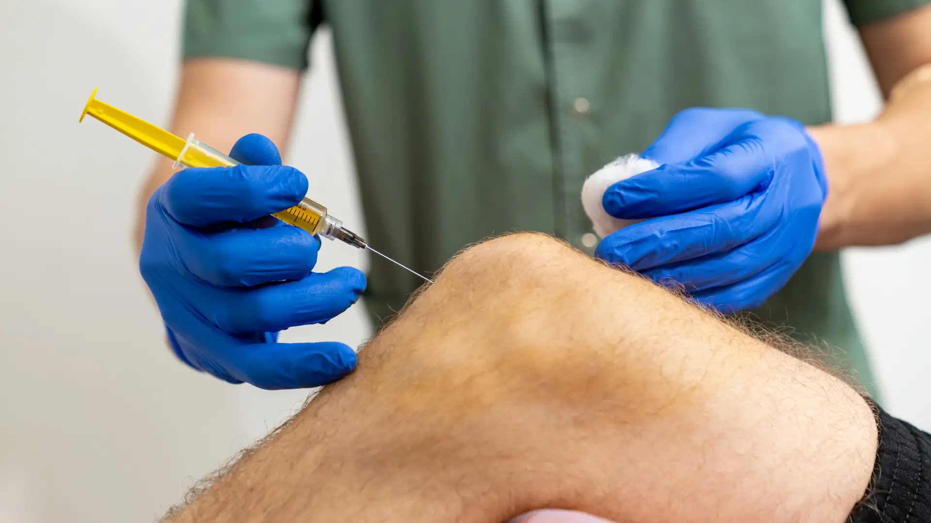 A medical professional administering a knee injection into a patient.