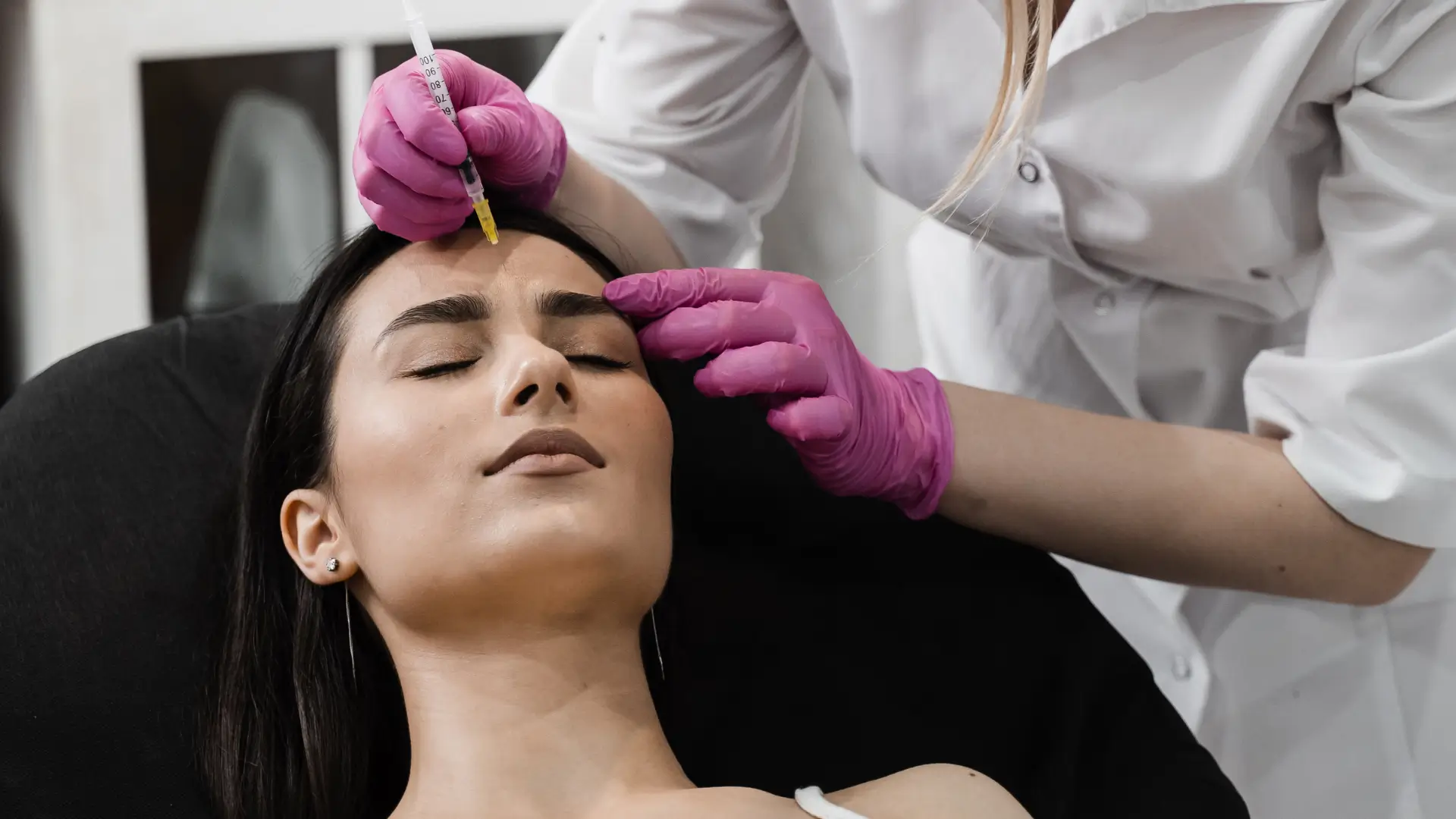 A medical professional administering an injection into a patient's frown lines.