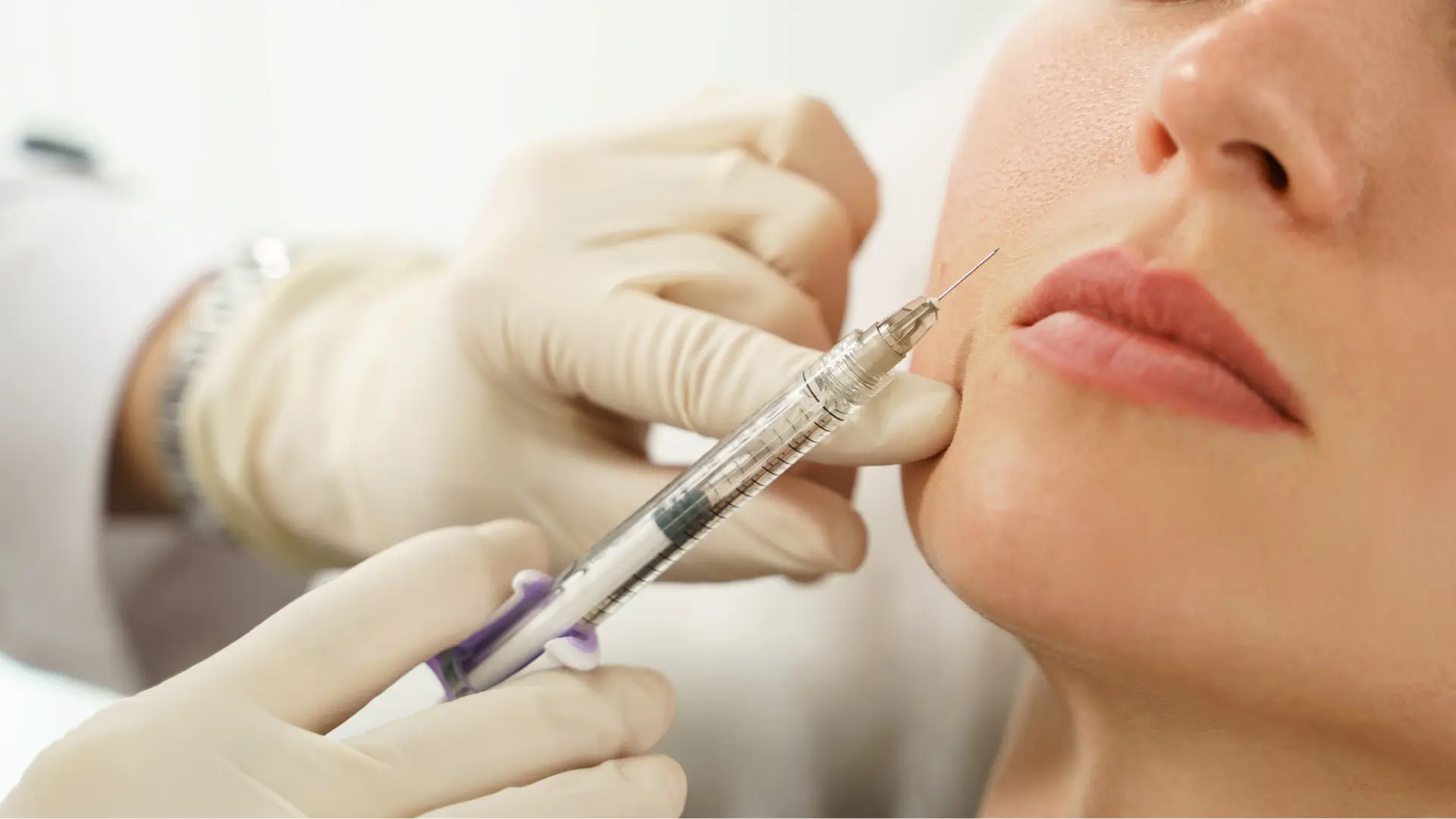 A medical professional preparing the administration of dermal filler into the patient's facial area.
