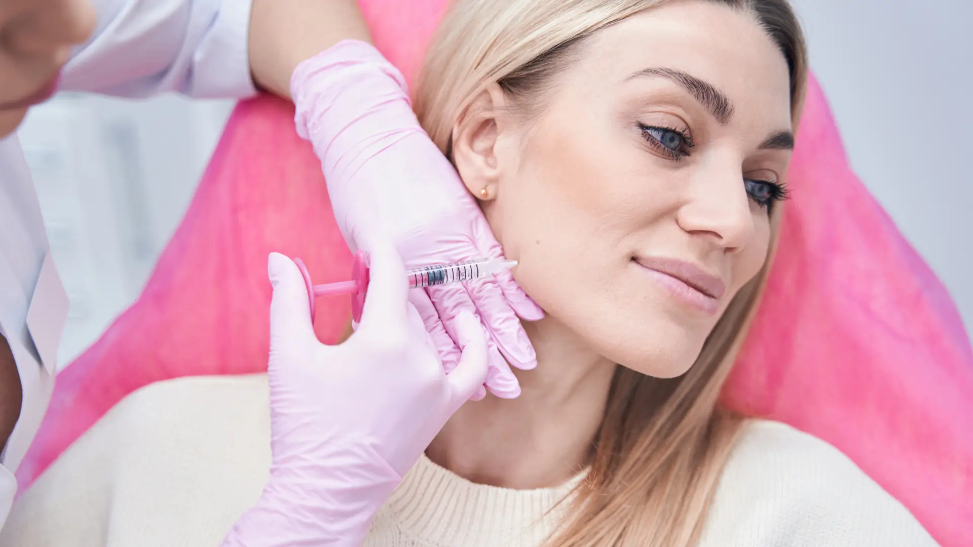 An aesthetic provider administering a dermal injection into a patient's jawline region.