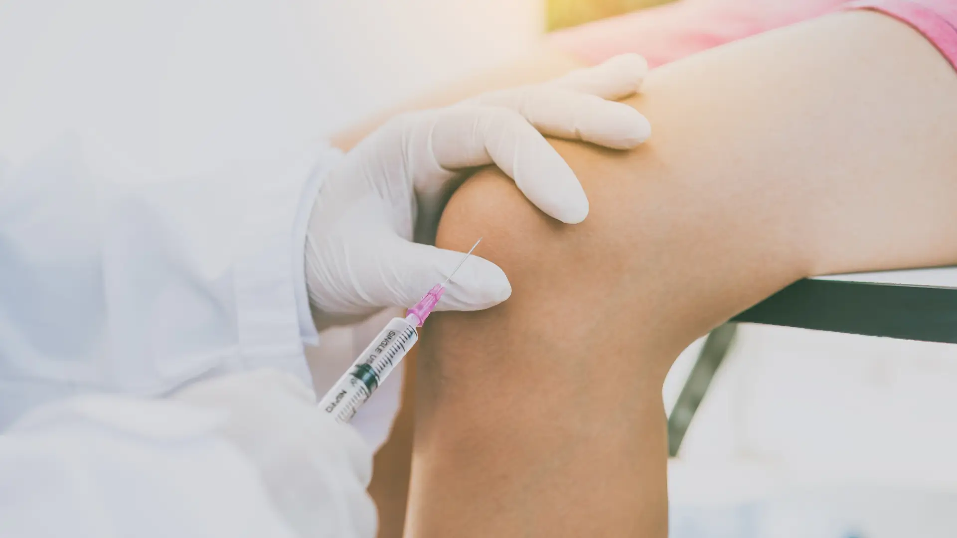A medical practitioner administering an injection into the patient's knee.