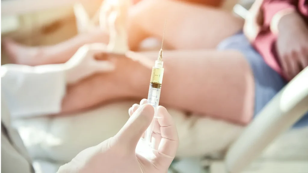 A medical professional holding an injection before injecting into a patient's knee.