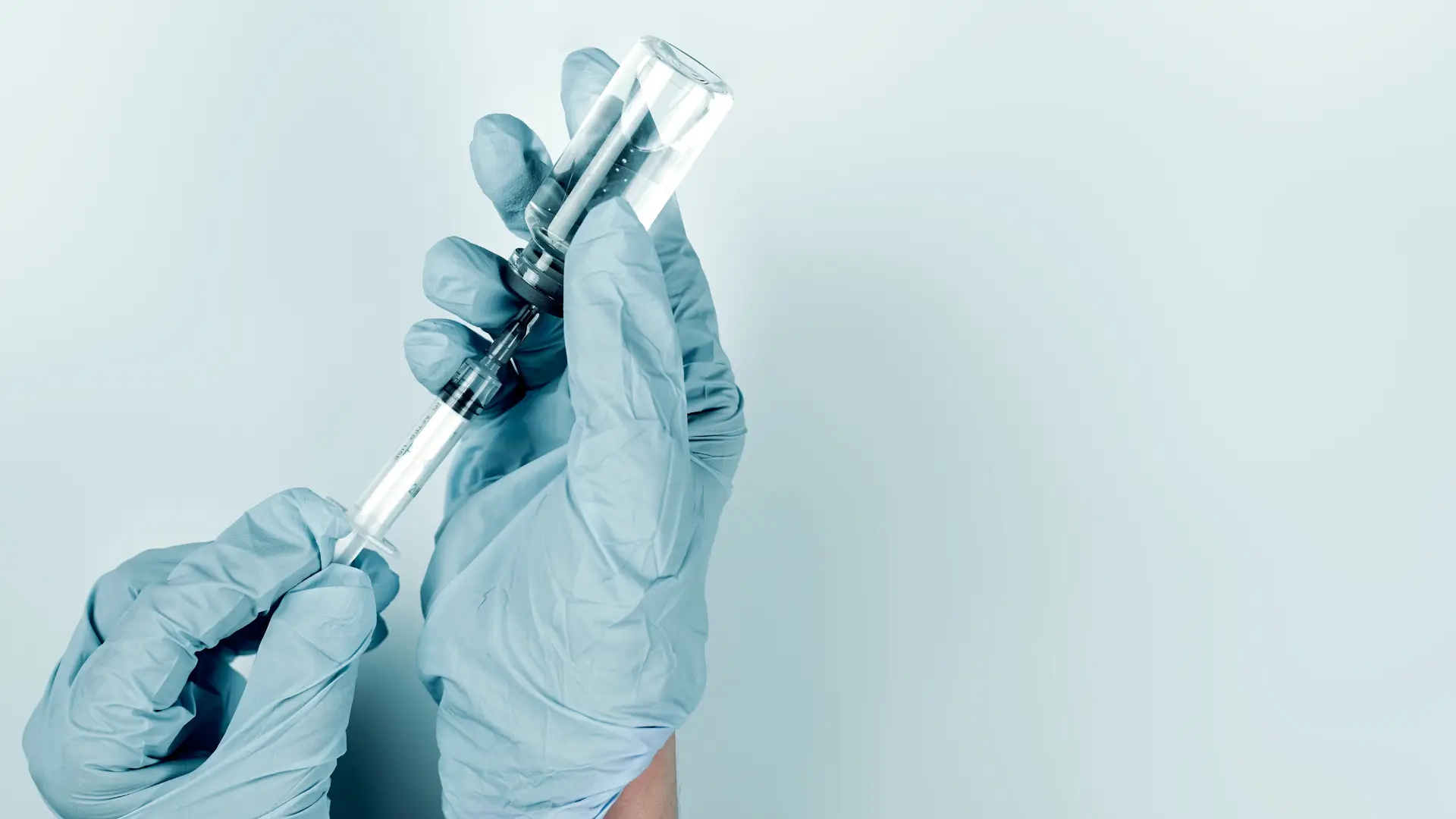 A medical professional transferring the vial's content into the syringe.