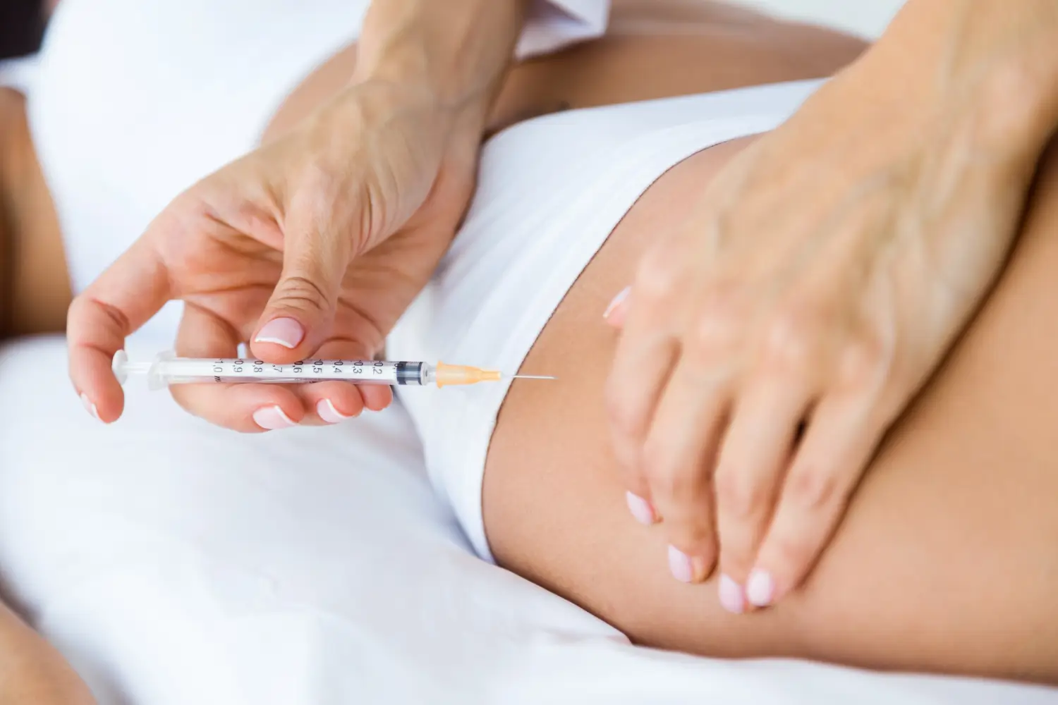 A medical professional administering an injection into a patient's thigh region.