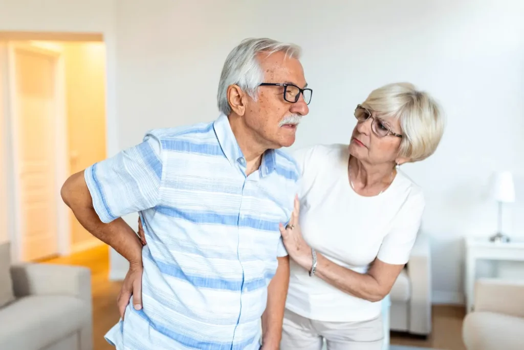 Elderly man dealing with back pain while his wife supports him.