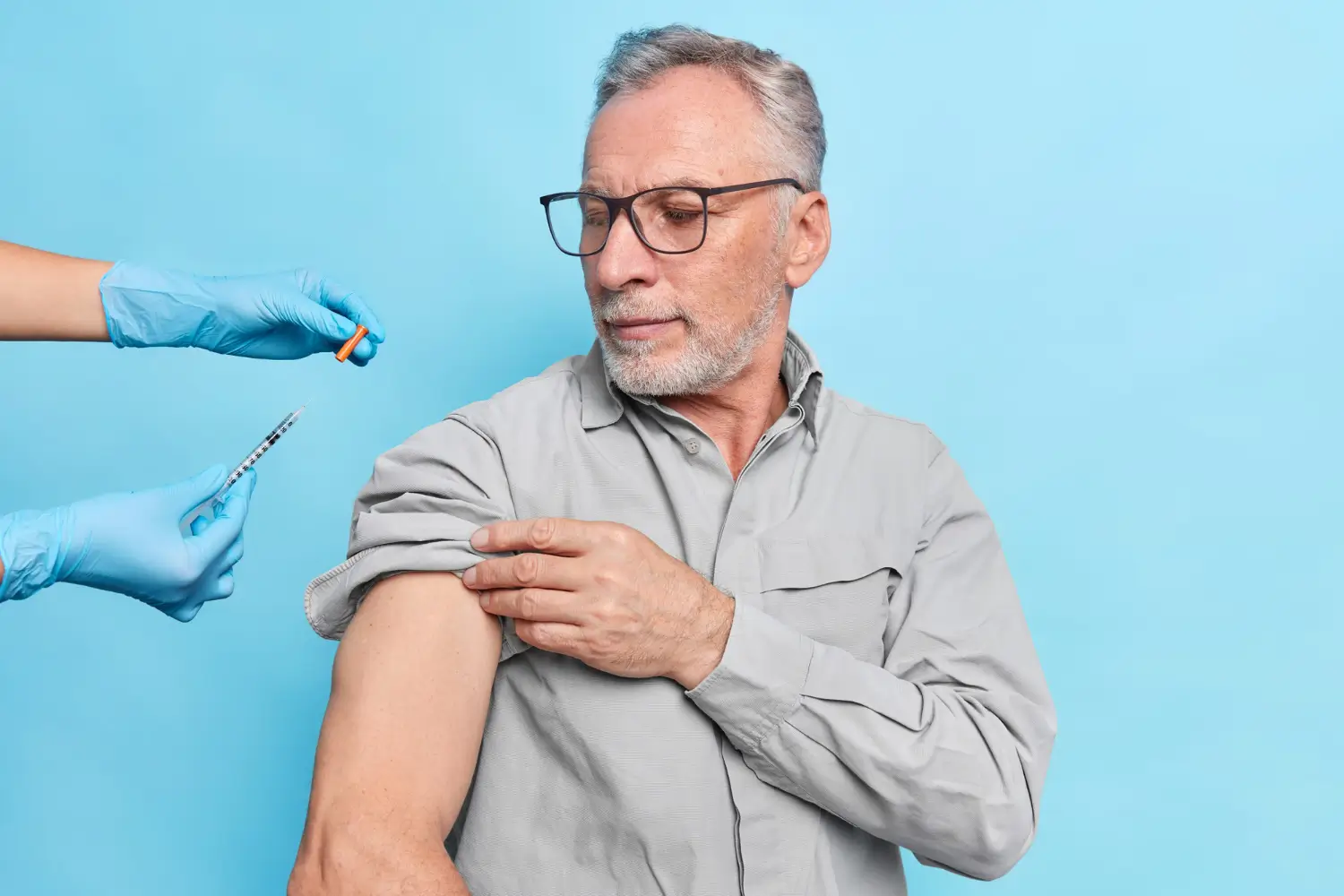 An older individual preparing to receive an injection in their upper arm.