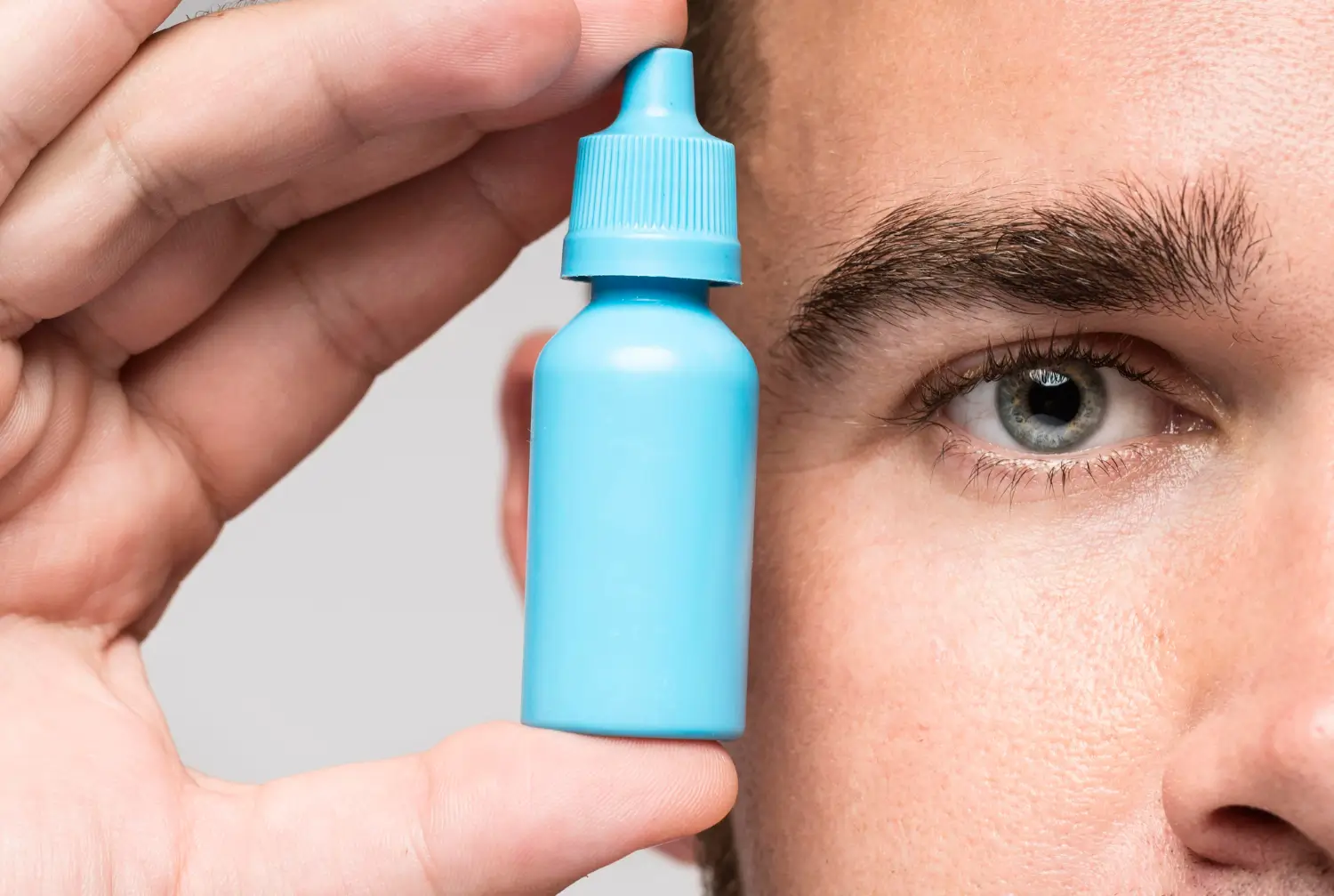An individual holding an eye drop bottle near the eyes.