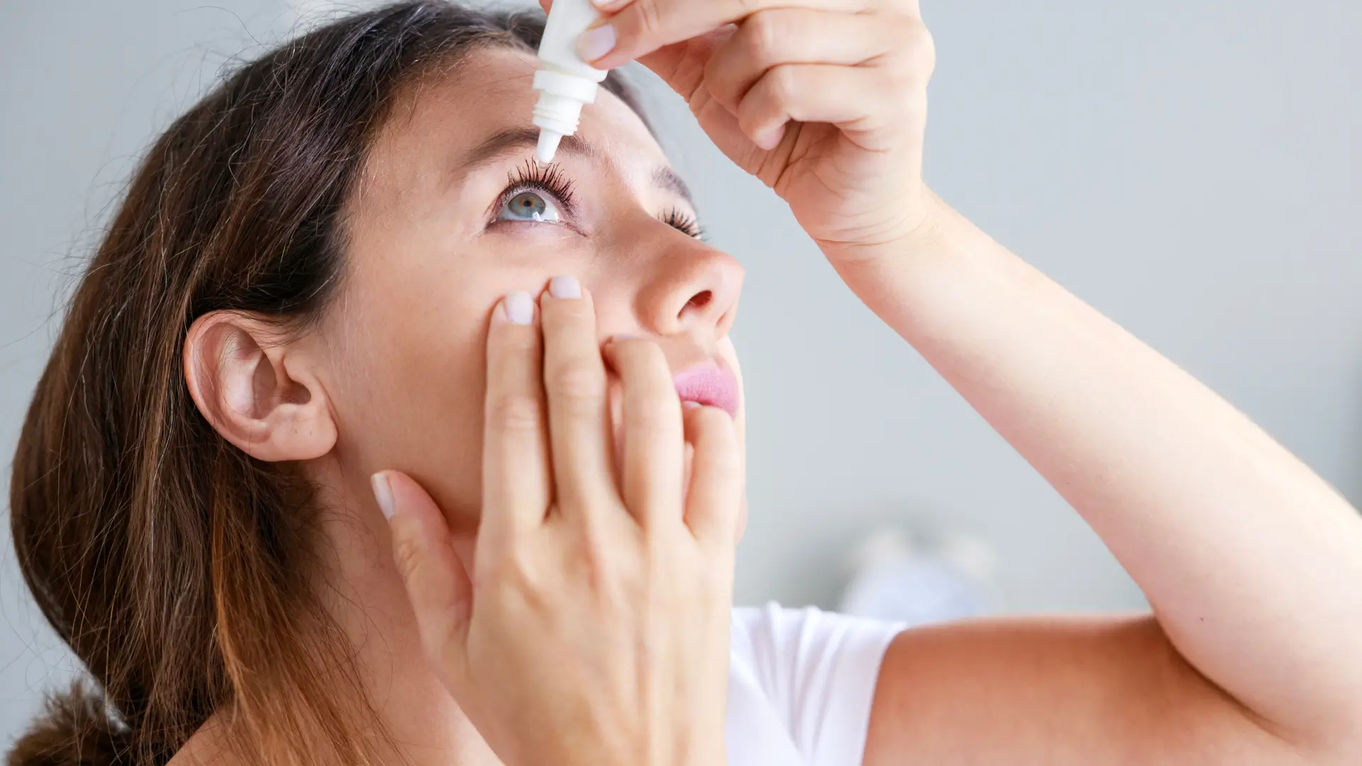 An individual applying eye drops in their eye.