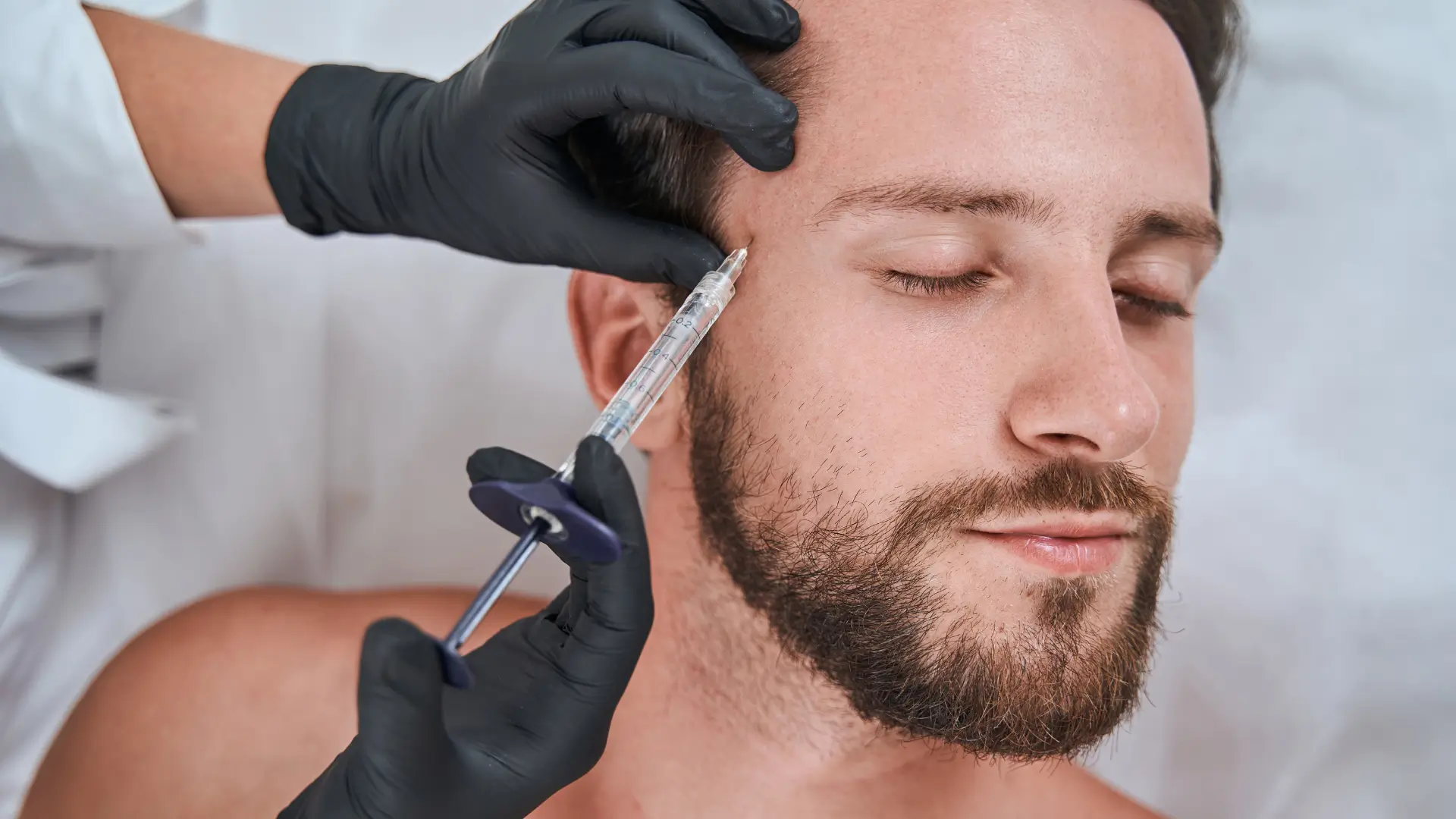 An individual receiving an injection into a patient's upper face region.