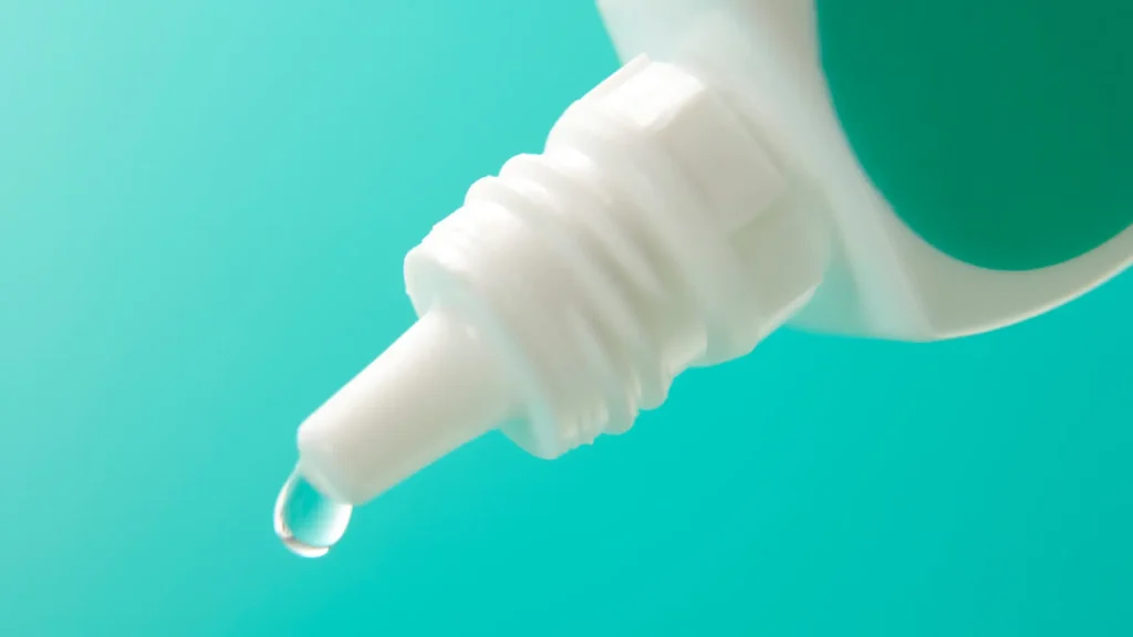 A close-up shot of an eye drop bottle and a drop.