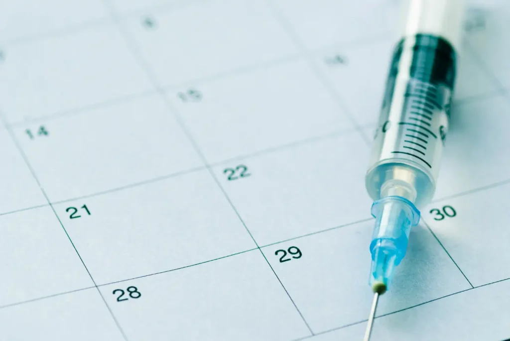 A medical syringe placed on top of a calendar.