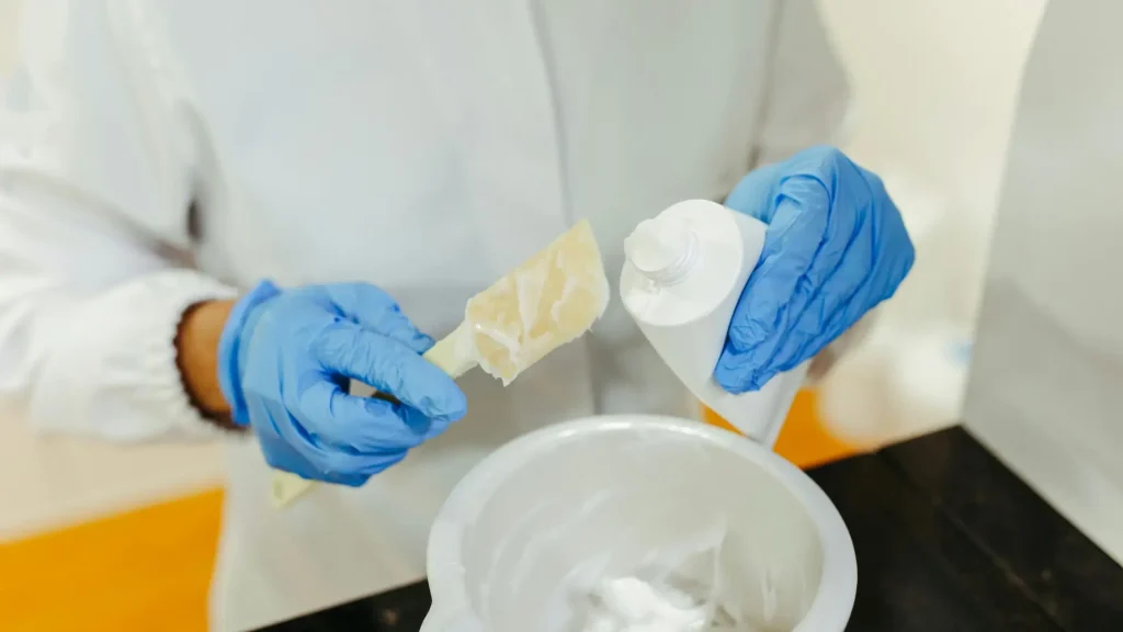 A medical professional transferring cream from a medicine tube to a container.