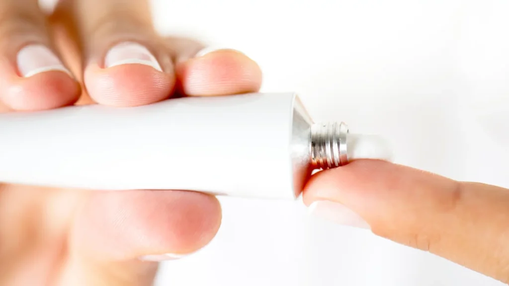 An individual squeezing the cream out of a medicine tube.
