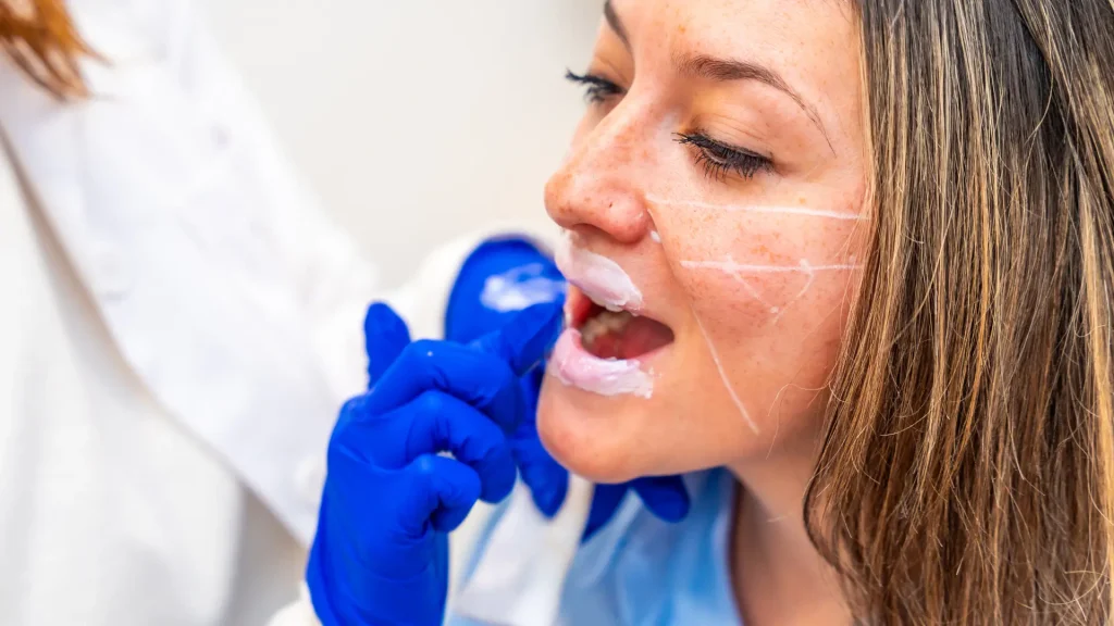 A medical professional applying topical anesthetic on a patient's lip.