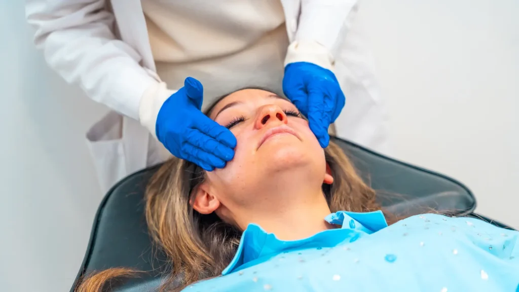 A doctor applying numbing cream on patient's face before treatment.