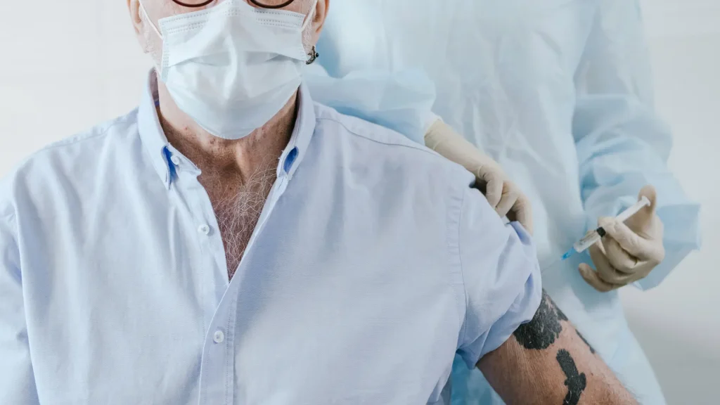 A male individual wearing a mask receiving an arm injection.