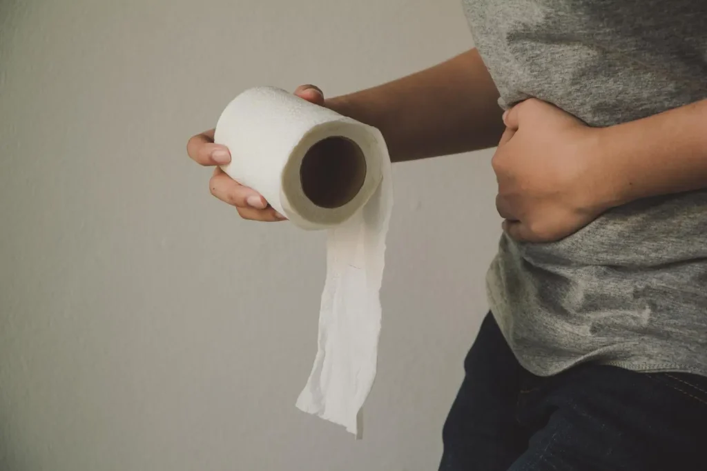 An individual dealing with stomach pain while holding a roll of tissue.