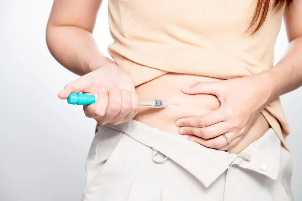 An individual administering an injection to their abdomen.