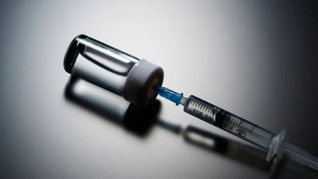 A vial and syringe on a dark surface.