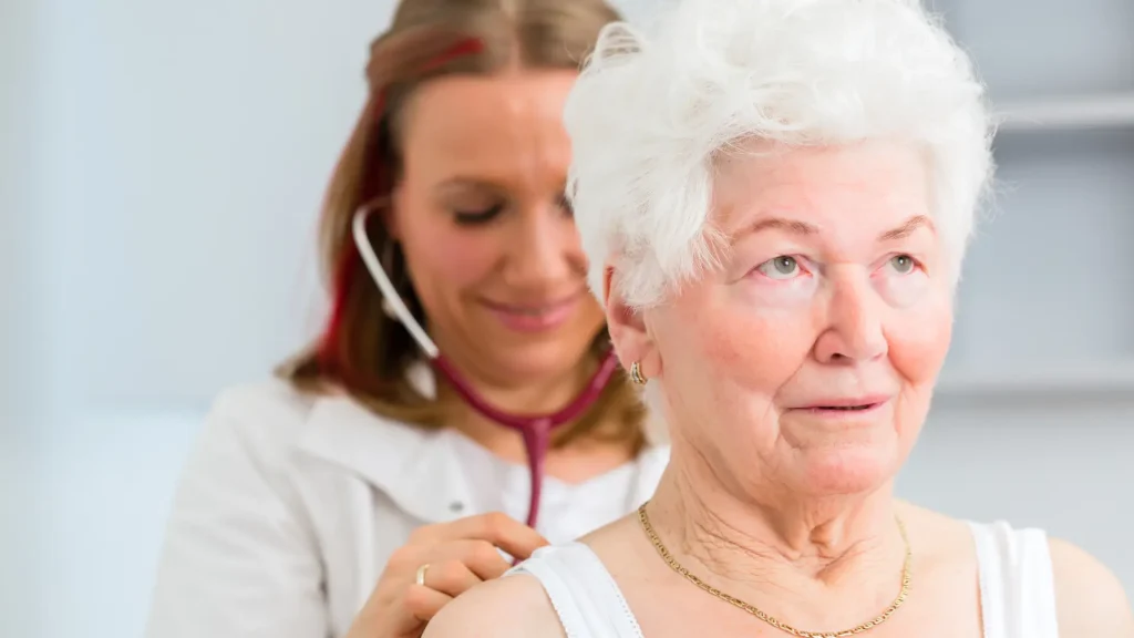 A medical professional auscultating an older female patient.